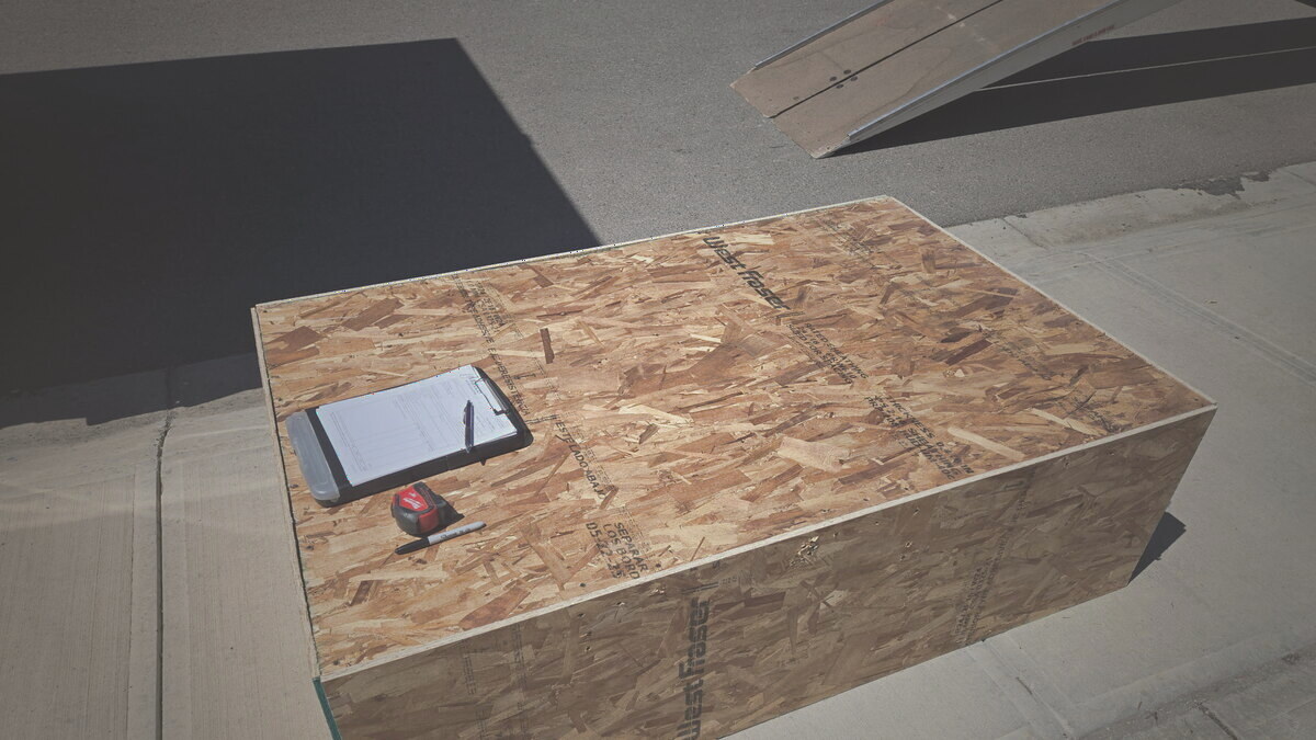 A clipboard and tape measure resting on a finished wood crate — every build is measured and documented first
