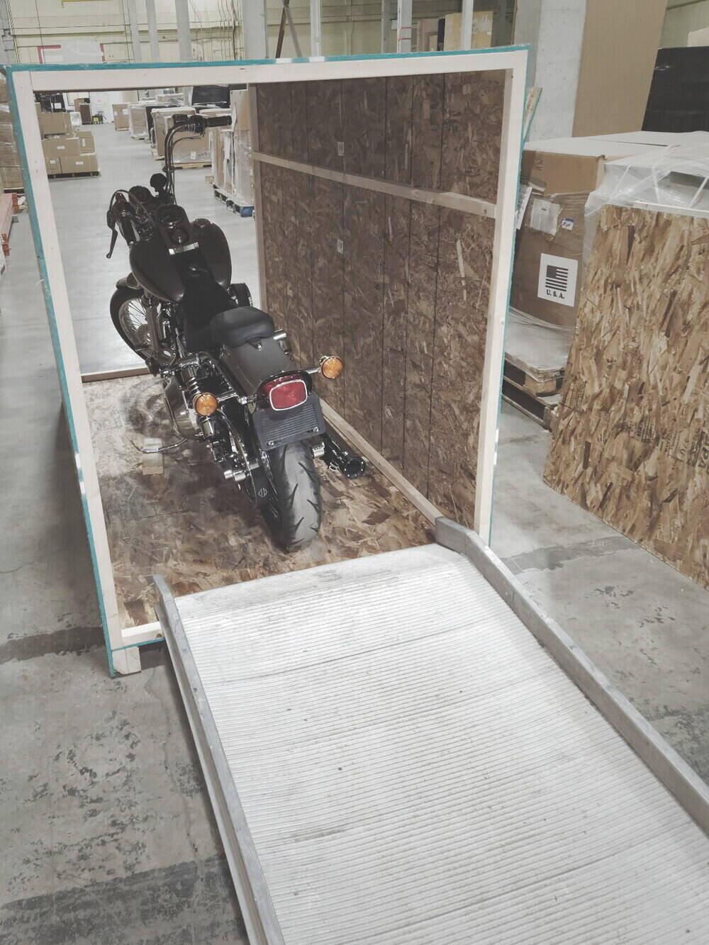 A motorcycle strapped on the deck of an open crate with the loading ramp down
