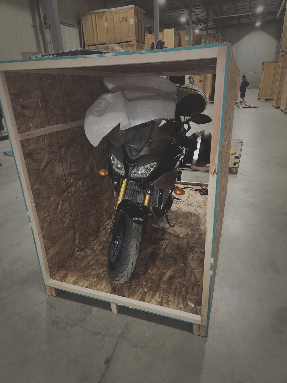 A Yamaha adventure motorcycle standing inside a custom wood crate, windscreen bubble-wrapped, ready to brace