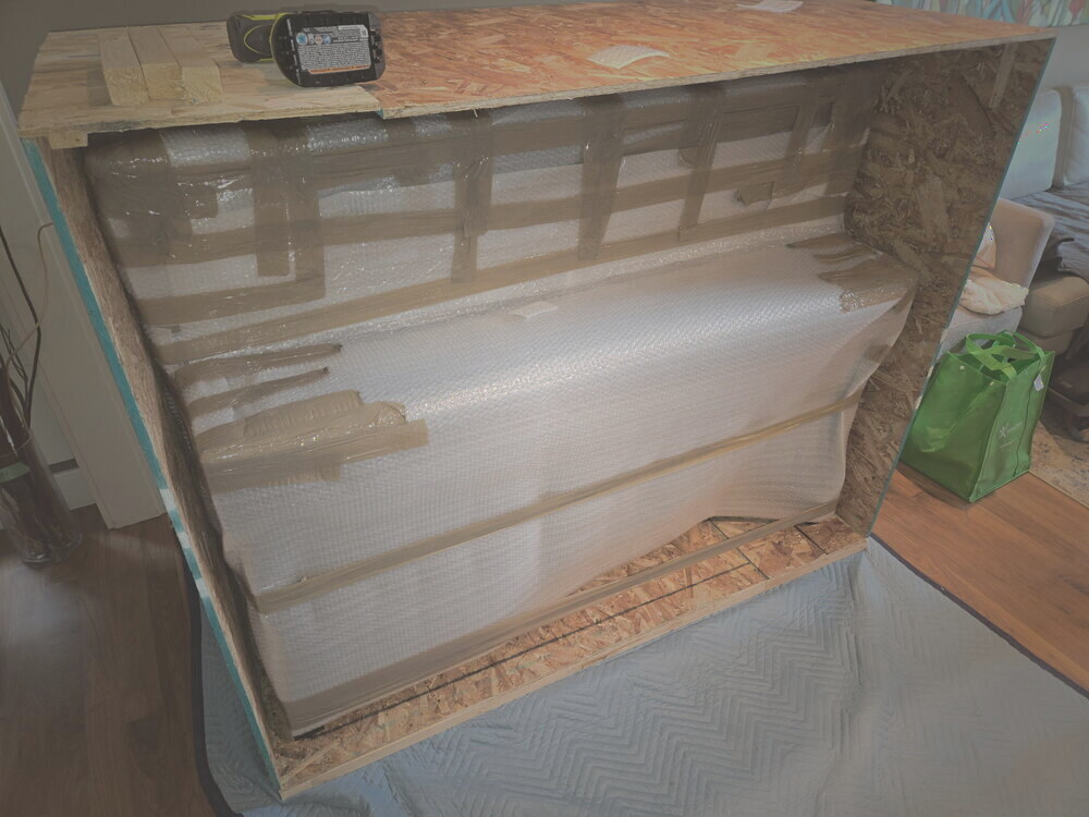An upright piano laid back, bubble-wrapped and braced inside an open wood crate
