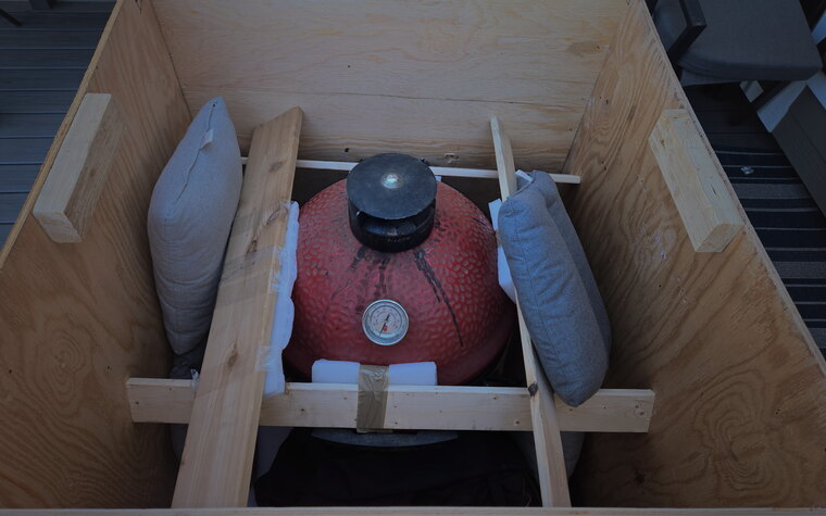 A red ceramic kamado grill cushioned and cross-braced inside a custom wood crate