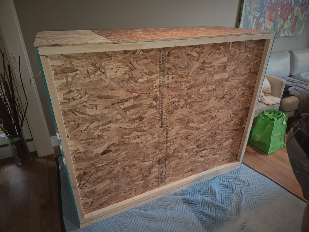 A sealed wood crate built around a large flat-screen television, standing in a client's living room