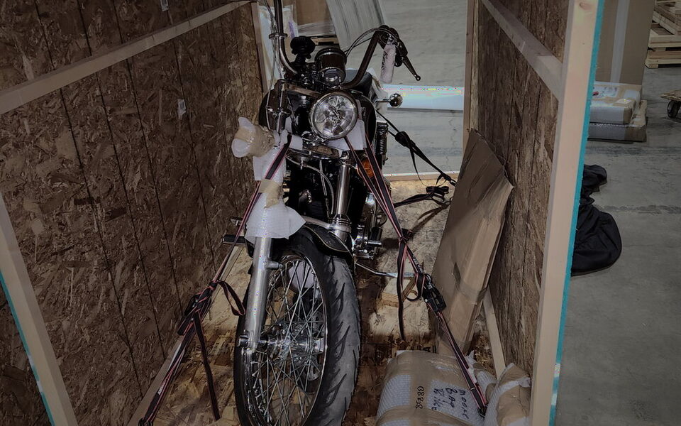 A chrome custom chopper braced and strapped upright inside an open crate.