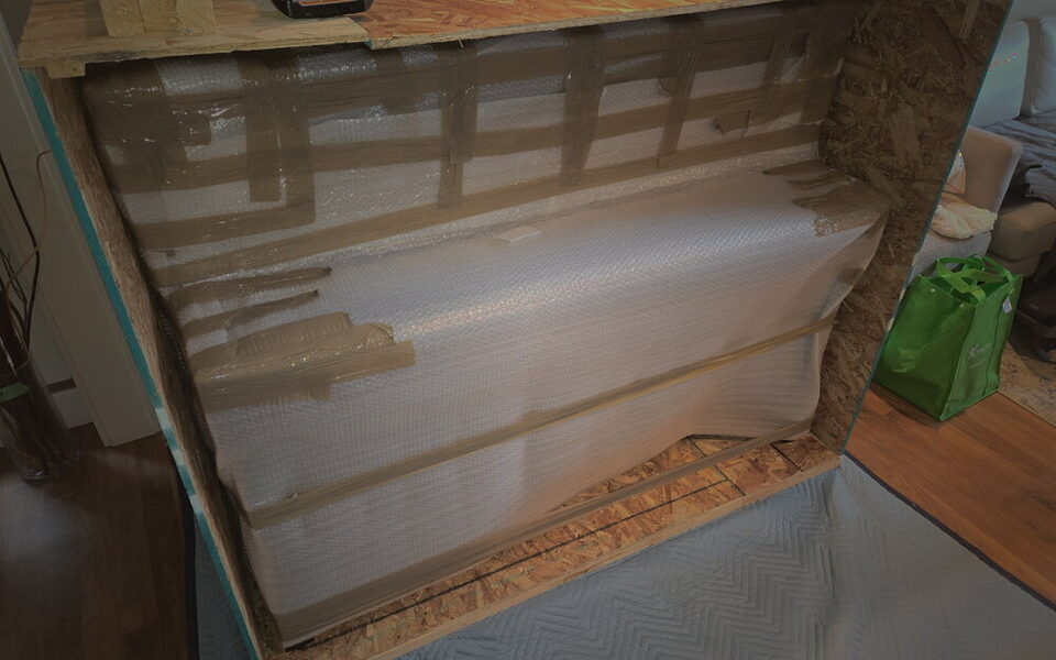 An upright piano laid back, bubble-wrapped and cross-braced inside an open custom crate in the client's living room.